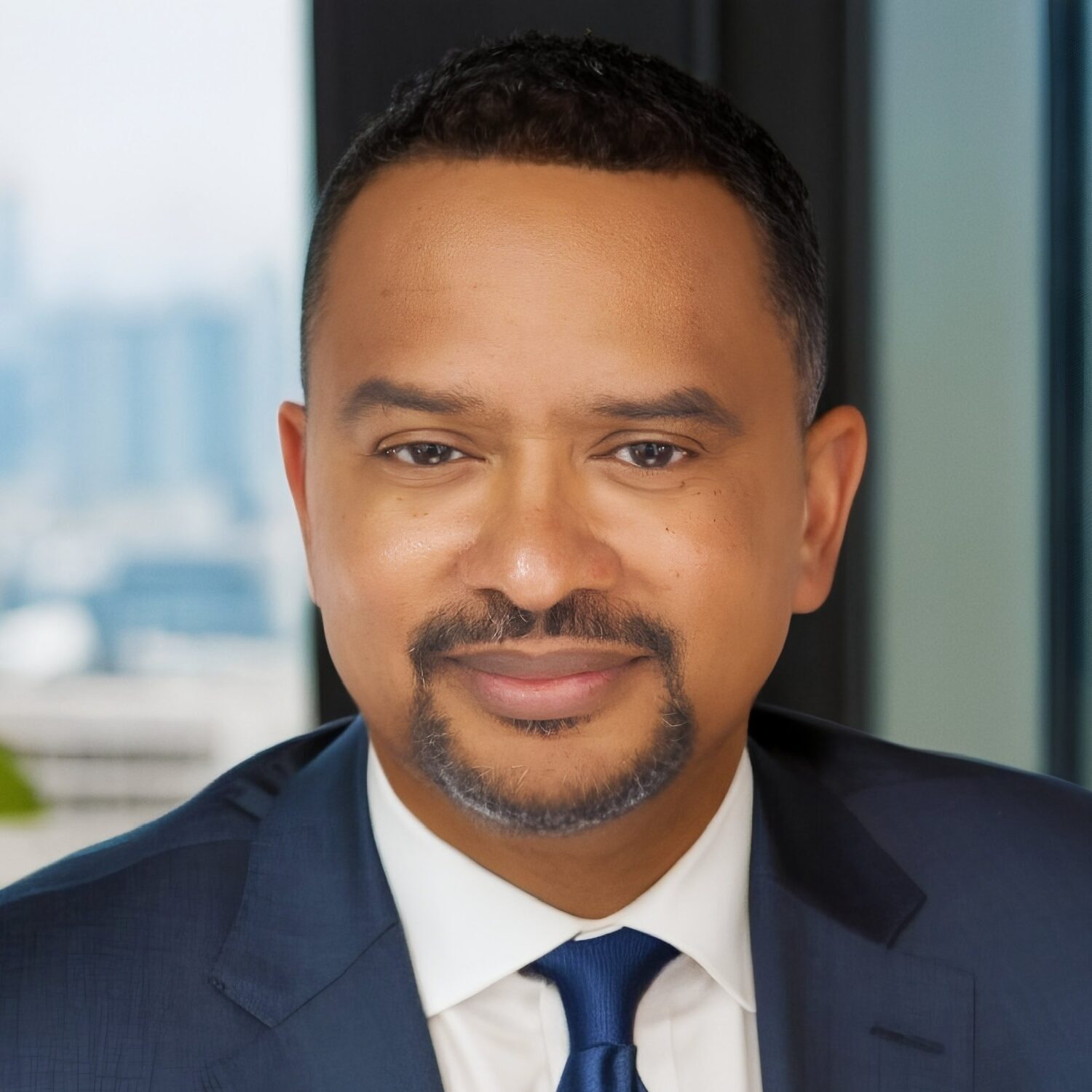 head and shoulder photo of Keith Scott with an office window in the background. Keith is wearing a white shirt, blue tie, and dark blue blazer