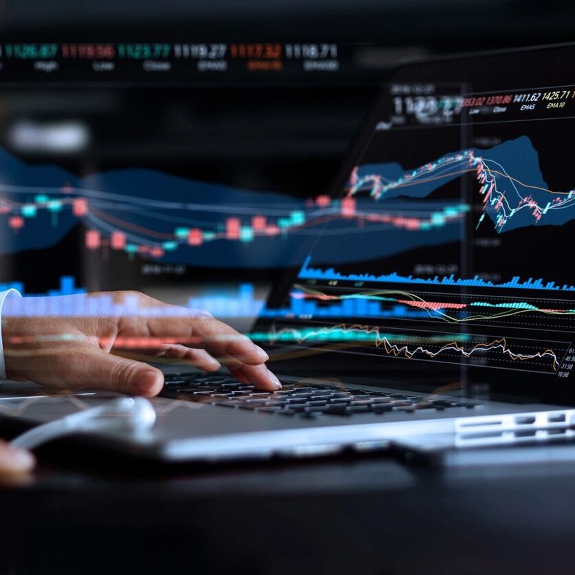 Typing on laptop view of hands typing on a laptop. the screen of the laptop shows financial line graphs and charts and the image effect shows the financial info has come out of the computer into the open space