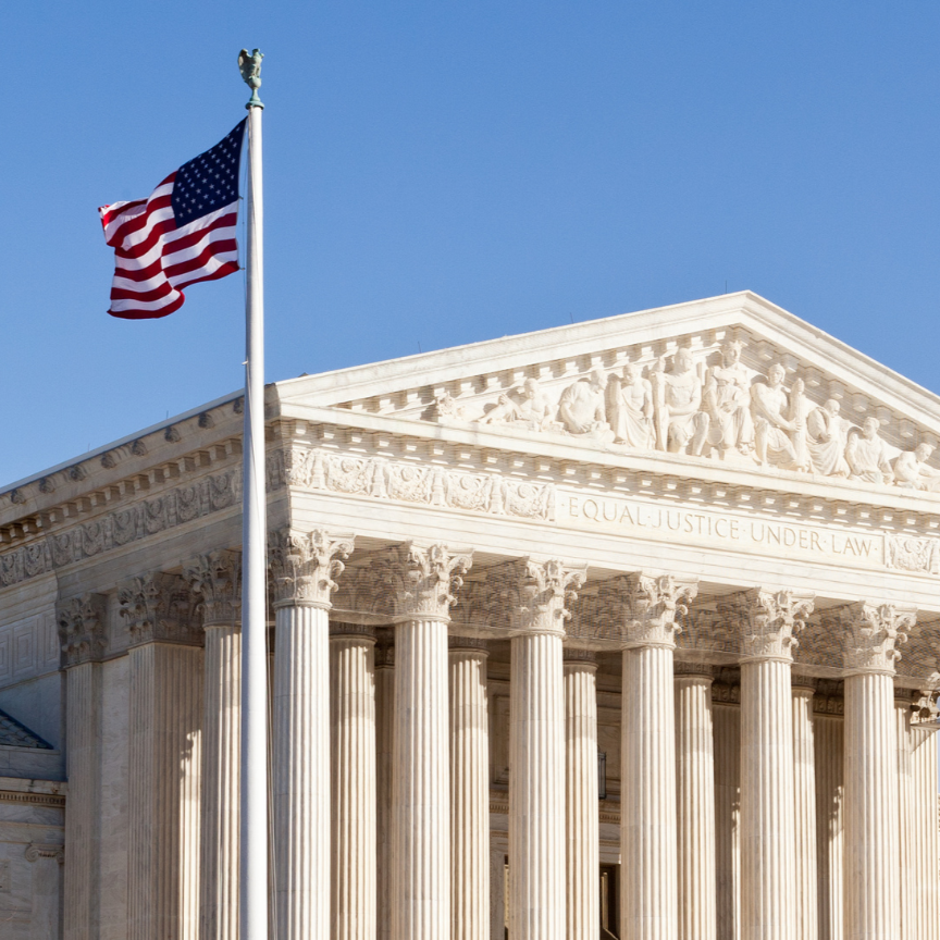 outside photo of the Supreme Court, a large white marble building with a triangular pointed roof and large columns. an American flag flies to the left of the court.